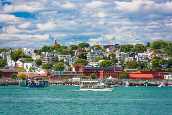Scenic view of Portland, Maine with colorful buildings, boats on blue water, and green trees under a partly cloudy sky.